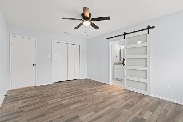 unfurnished bedroom with a closet, wood-type flooring, ensuite bathroom, ceiling fan, and a barn door