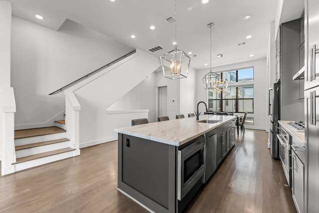 kitchen with appliances with stainless steel finishes, hanging light fixtures, an island with sink, light stone countertops, and sink