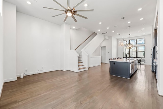 kitchen with sink, ceiling fan with notable chandelier, dark hardwood / wood-style flooring, hanging light fixtures, and an island with sink