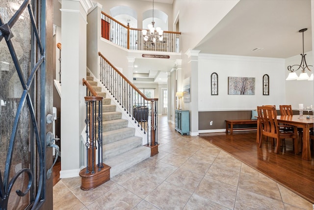 tiled foyer with baseboards, stairway, ornamental molding, ornate columns, and a notable chandelier