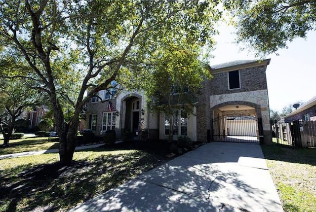 view of front of house featuring stone siding, fence, concrete driveway, and a gate