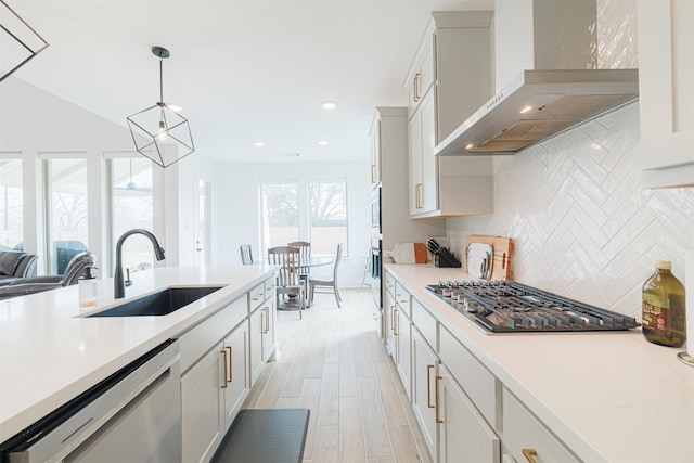 kitchen featuring white cabinetry, sink, appliances with stainless steel finishes, wall chimney exhaust hood, and pendant lighting