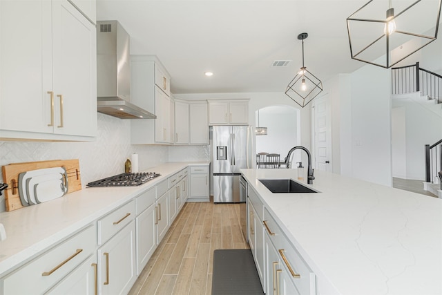 kitchen featuring sink, pendant lighting, stainless steel appliances, wall chimney exhaust hood, and white cabinets