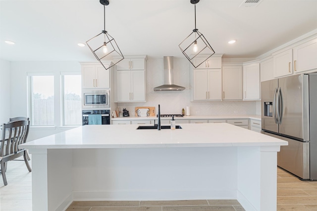 kitchen with white cabinetry, wall chimney range hood, stainless steel appliances, and an island with sink