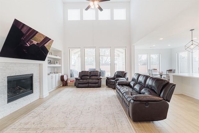 living room with light wood-type flooring, ceiling fan, built in features, and a fireplace