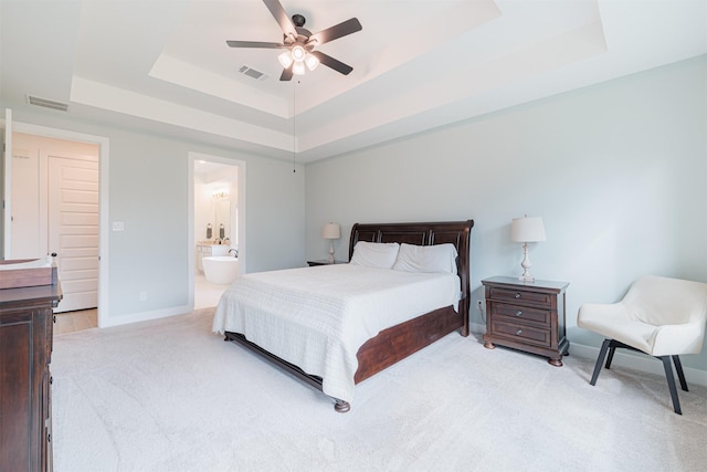 bedroom featuring a raised ceiling, ensuite bathroom, light carpet, and ceiling fan