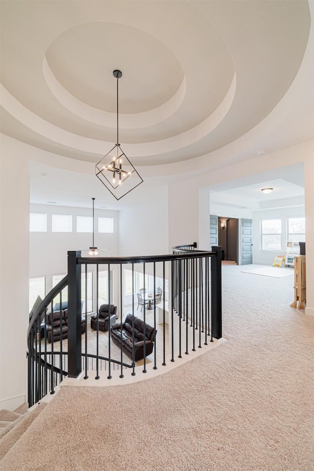 corridor with a tray ceiling, carpet, and an inviting chandelier