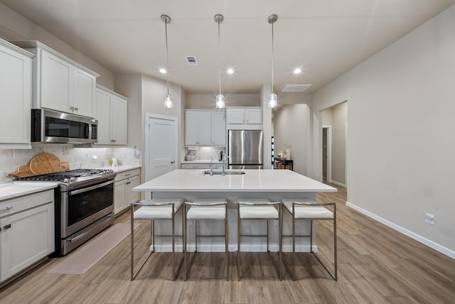 kitchen with a kitchen breakfast bar, a center island with sink, appliances with stainless steel finishes, and hanging light fixtures