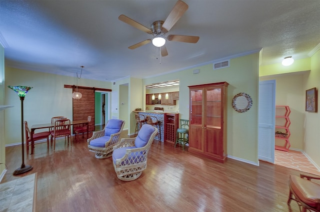 sitting room with a barn door, light hardwood / wood-style floors, ornamental molding, ceiling fan, and a textured ceiling