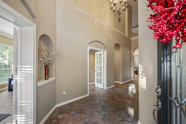 entrance foyer with arched walkways, a towering ceiling, an inviting chandelier, stone finish floor, and baseboards