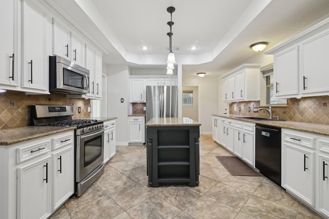 kitchen with white cabinetry, stainless steel appliances, a center island, light stone countertops, and a tray ceiling