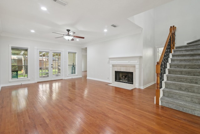 unfurnished living room with wood-type flooring, french doors, ceiling fan, a fireplace, and ornamental molding