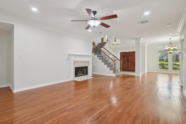 unfurnished living room with ceiling fan with notable chandelier, light hardwood / wood-style flooring, a tile fireplace, and crown molding