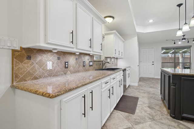 kitchen with tasteful backsplash, hanging light fixtures, light stone counters, sink, and white cabinetry