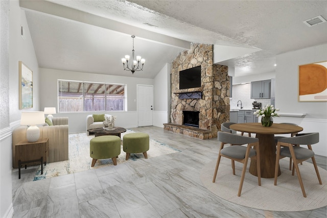 living room featuring a textured ceiling, lofted ceiling with beams, a fireplace, sink, and an inviting chandelier