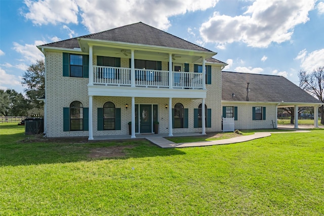 rear view of property with ceiling fan, brick siding, a lawn, and a balcony