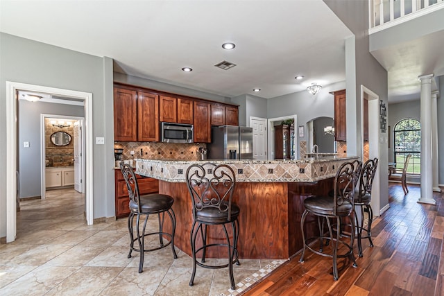 kitchen featuring arched walkways, stainless steel appliances, visible vents, decorative backsplash, and decorative columns