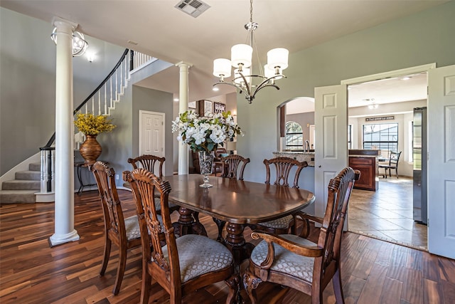 dining room featuring dark wood-style flooring, decorative columns, a notable chandelier, visible vents, and stairway