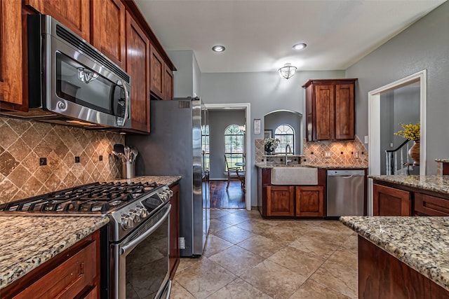 kitchen featuring light stone counters, arched walkways, tasteful backsplash, appliances with stainless steel finishes, and a sink