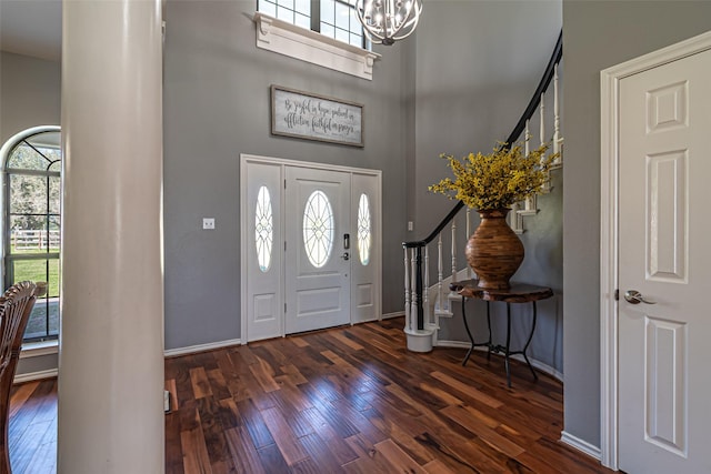 entryway featuring a chandelier, dark wood-type flooring, a towering ceiling, baseboards, and stairs