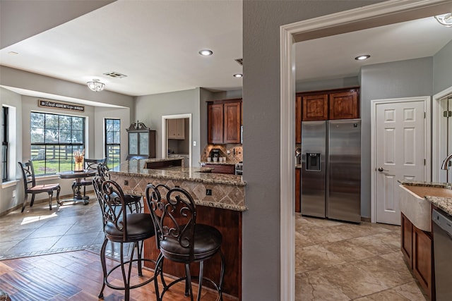 kitchen featuring visible vents, dishwasher, stainless steel fridge with ice dispenser, a breakfast bar, and a sink