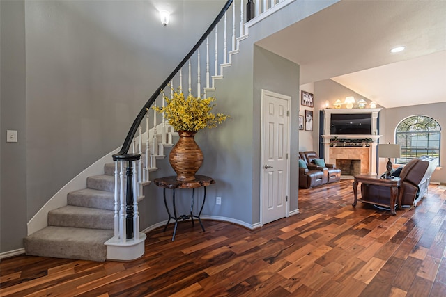 stairway with high vaulted ceiling, a fireplace, wood finished floors, and baseboards