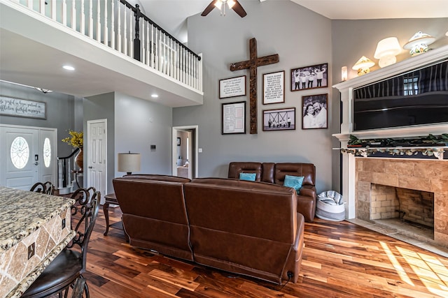 living room with a towering ceiling, a fireplace, a ceiling fan, and dark wood-style flooring