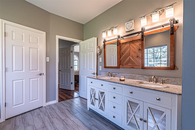 bathroom featuring double vanity, wood finished floors, a sink, and baseboards