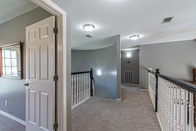 corridor with carpet floors, visible vents, and an upstairs landing