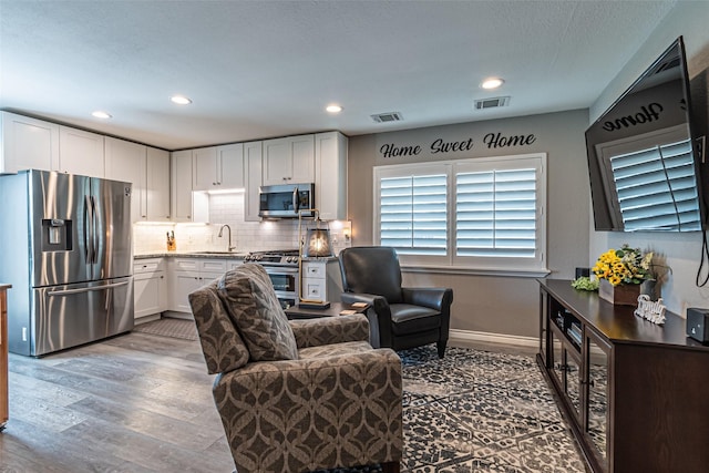 living area with recessed lighting, wood finished floors, visible vents, and baseboards