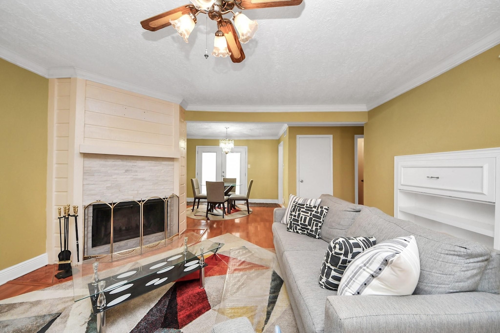 living room featuring hardwood / wood-style flooring, ceiling fan, crown molding, and a textured ceiling