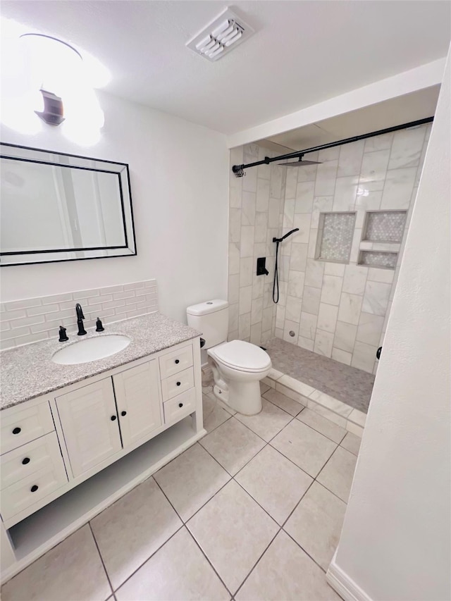 bathroom with visible vents, toilet, tile patterned floors, a tile shower, and backsplash