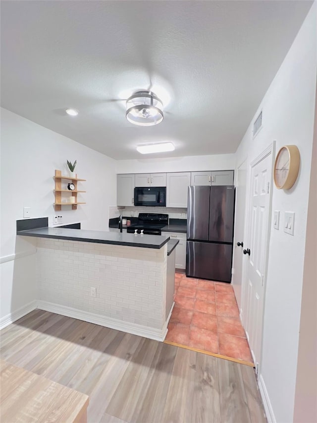 kitchen featuring visible vents, dark countertops, light wood-style flooring, a peninsula, and black appliances