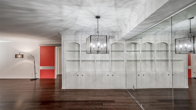 unfurnished dining area featuring dark wood-type flooring, crown molding, and a chandelier