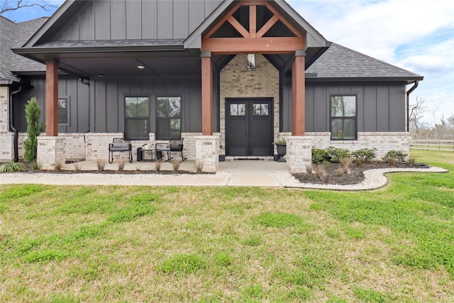 view of front facade with covered porch, stone siding, roof with shingles, a front lawn, and board and batten siding