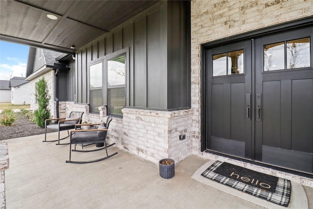 entrance to property with french doors, brick siding, covered porch, board and batten siding, and stone siding