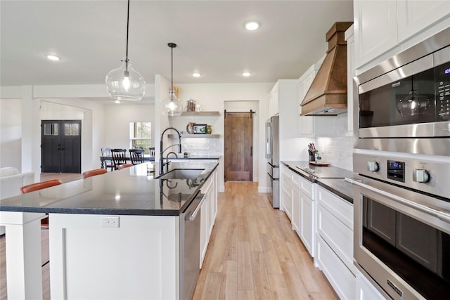 kitchen with a barn door, a sink, custom exhaust hood, a center island with sink, and pendant lighting