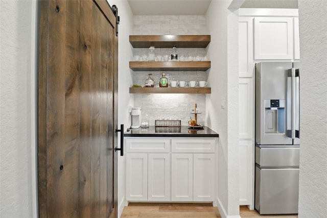 bar featuring backsplash, a barn door, light wood-style floors, a bar, and stainless steel fridge