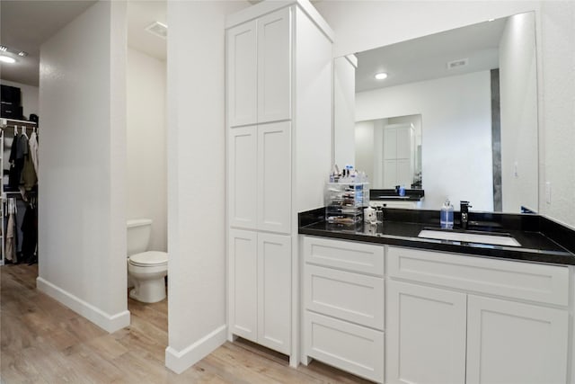 full bath featuring a spacious closet, toilet, vanity, wood finished floors, and baseboards