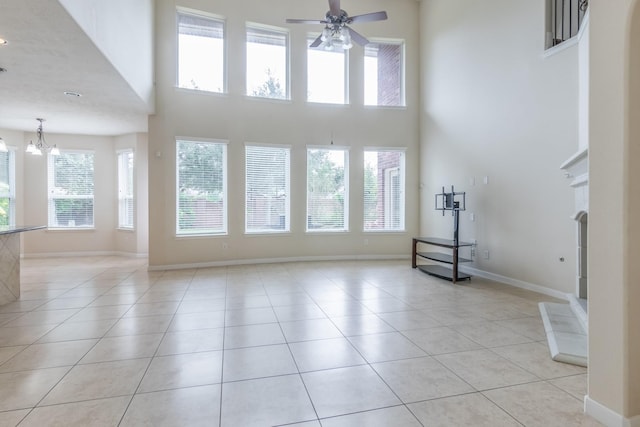 unfurnished living room featuring light tile patterned flooring, ceiling fan with notable chandelier, and a towering ceiling