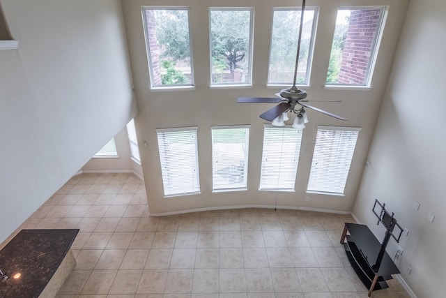 unfurnished living room with light tile patterned flooring, plenty of natural light, ceiling fan, and a high ceiling