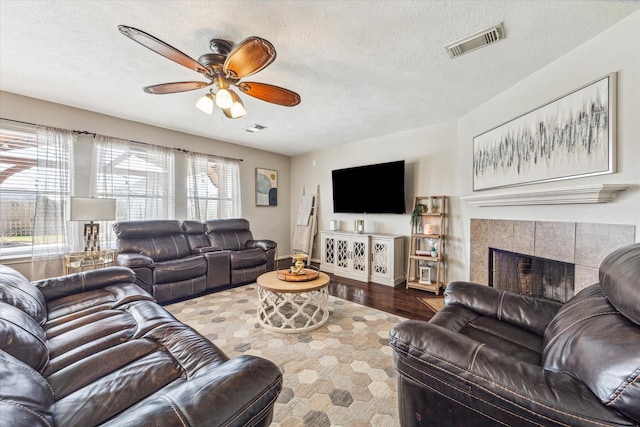 living room featuring hardwood / wood-style floors, a tiled fireplace, ceiling fan, and a textured ceiling