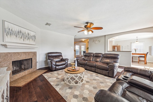 living room with dark hardwood / wood-style flooring, ceiling fan, a textured ceiling, and a tiled fireplace