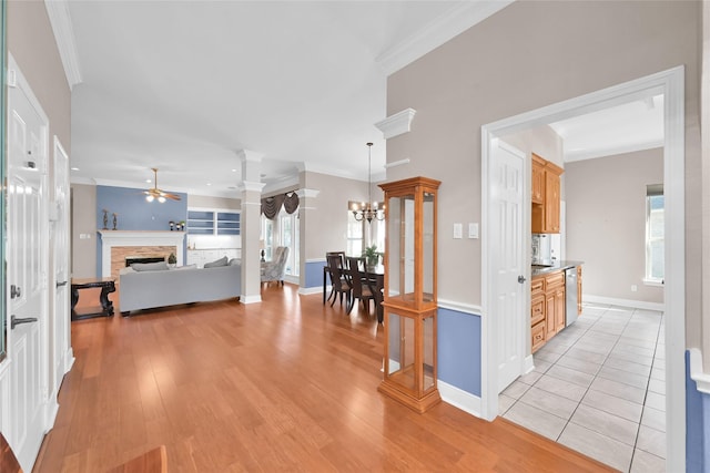 hall featuring crown molding, decorative columns, light wood-type flooring, baseboards, and a chandelier