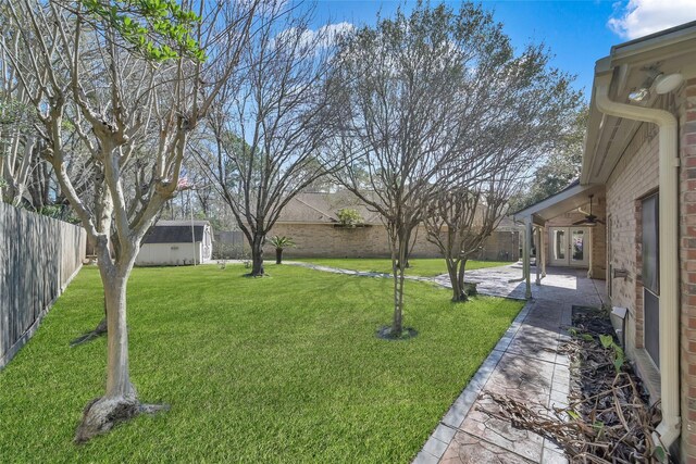 view of yard featuring a ceiling fan, a patio, an outdoor structure, a storage shed, and french doors
