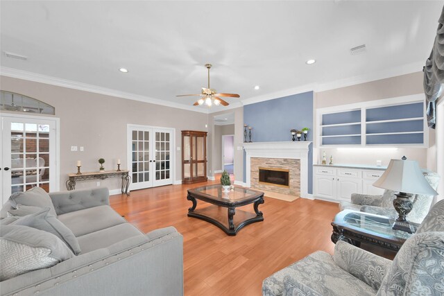 living room with french doors, light wood finished floors, a fireplace with flush hearth, ceiling fan, and ornamental molding