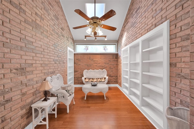 sitting room with brick wall, a ceiling fan, vaulted ceiling, and wood finished floors