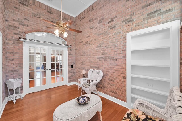 sitting room featuring brick wall, baseboards, french doors, wood finished floors, and a towering ceiling