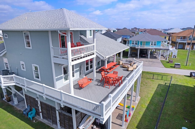 rear view of property featuring a shingled roof, a lawn, a residential view, a wooden deck, and an outdoor living space