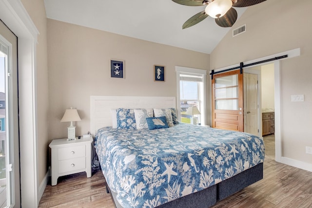 bedroom with vaulted ceiling, a barn door, wood finished floors, and visible vents